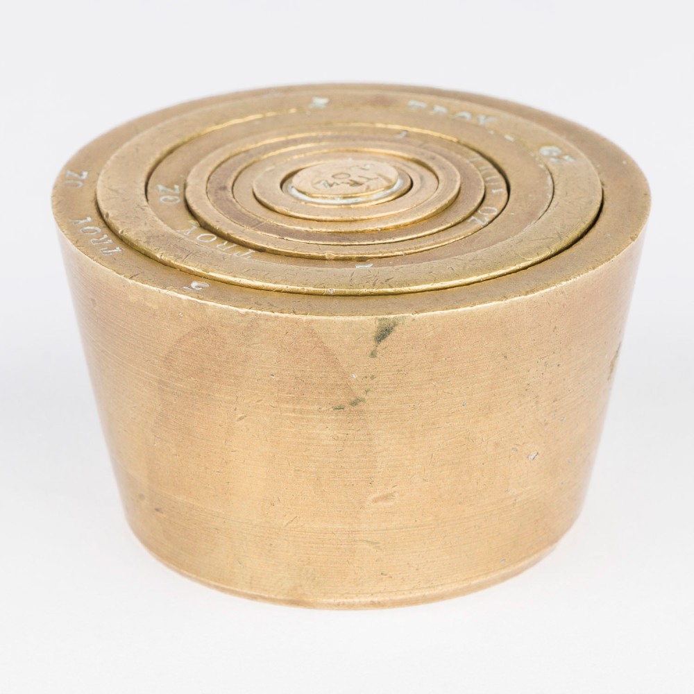 A set of eight graduated cylindrical brass nesting cup weights arranged in two loose rows on a plain white surface. View IV