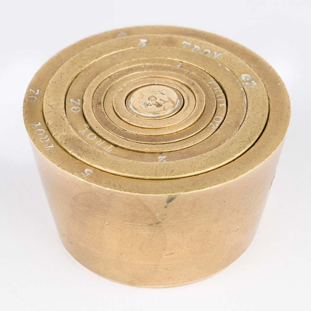 A set of eight graduated cylindrical brass nesting cup weights arranged in two loose rows on a plain white surface. View V