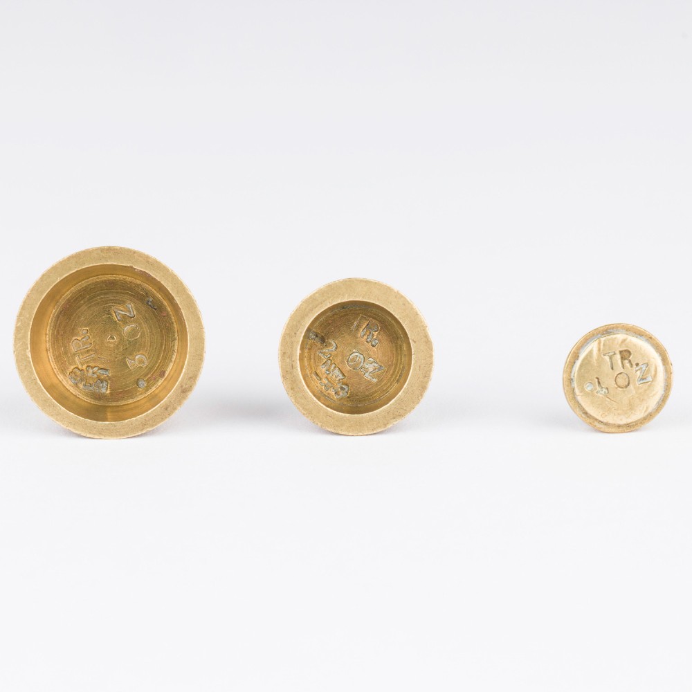 A set of eight graduated cylindrical brass nesting cup weights arranged in two loose rows on a plain white surface. View VIII