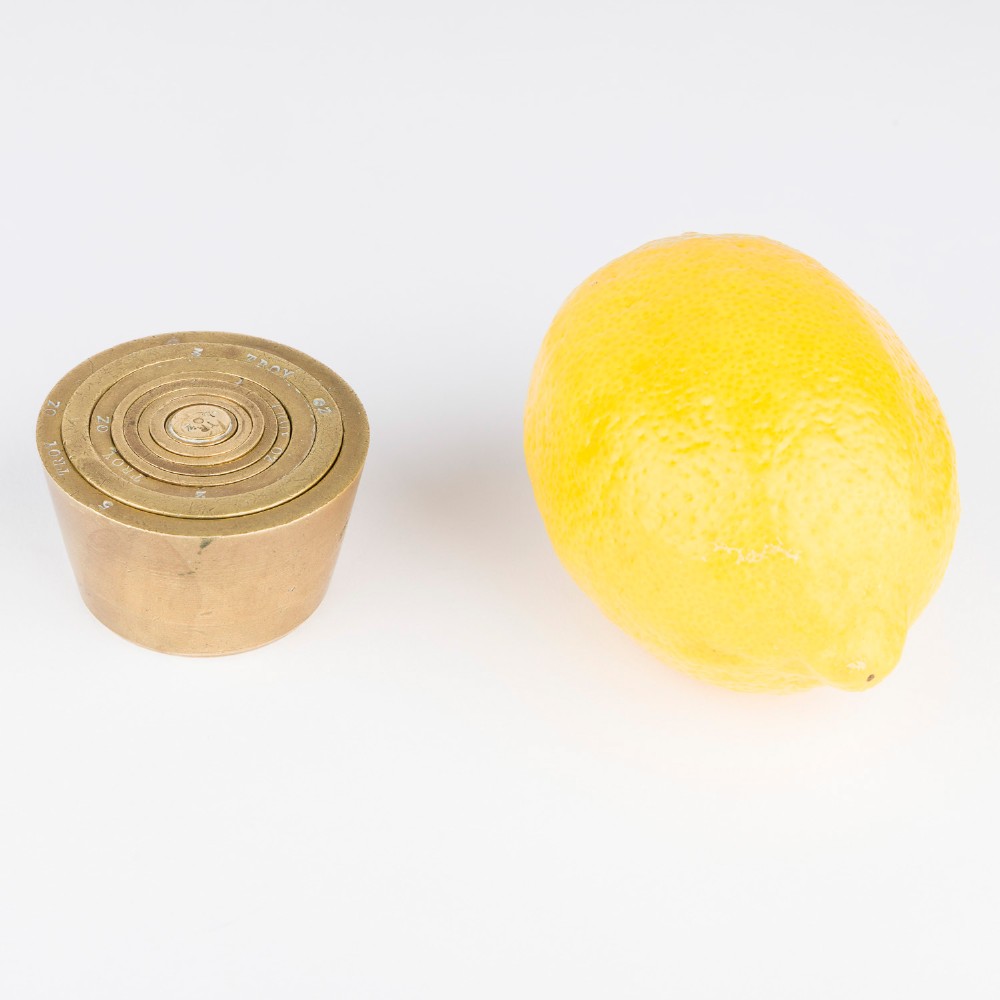 A set of eight graduated cylindrical brass nesting cup weights arranged in two loose rows on a plain white surface. View IX