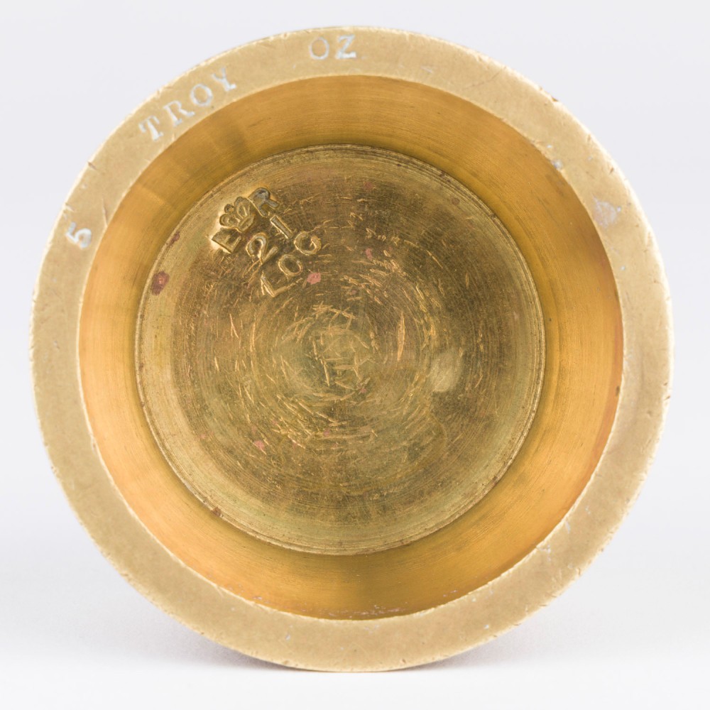 A set of eight graduated cylindrical brass nesting cup weights arranged in two loose rows on a plain white surface. View X