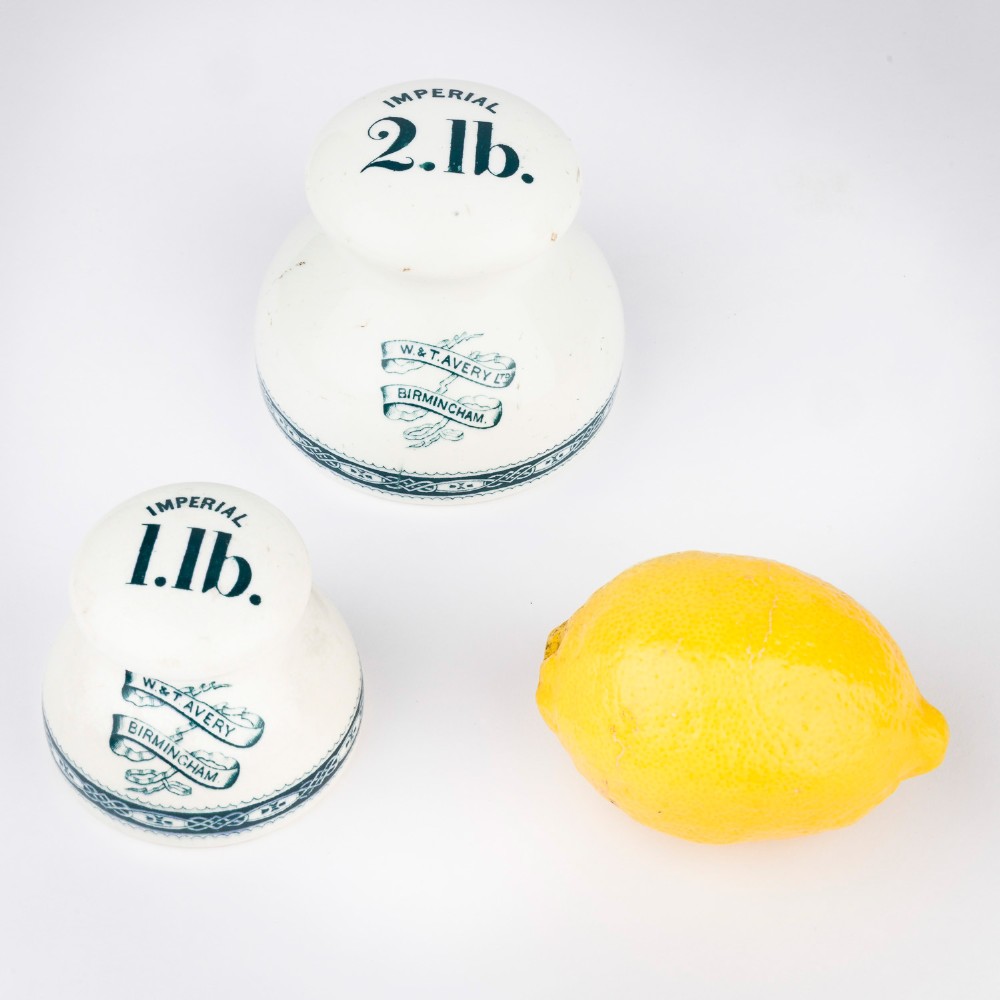 A pair of white glazed ceramic shop scale weights decorated with blue transfer-printed text and scroll borders for W and T Avery Birmingham. View X