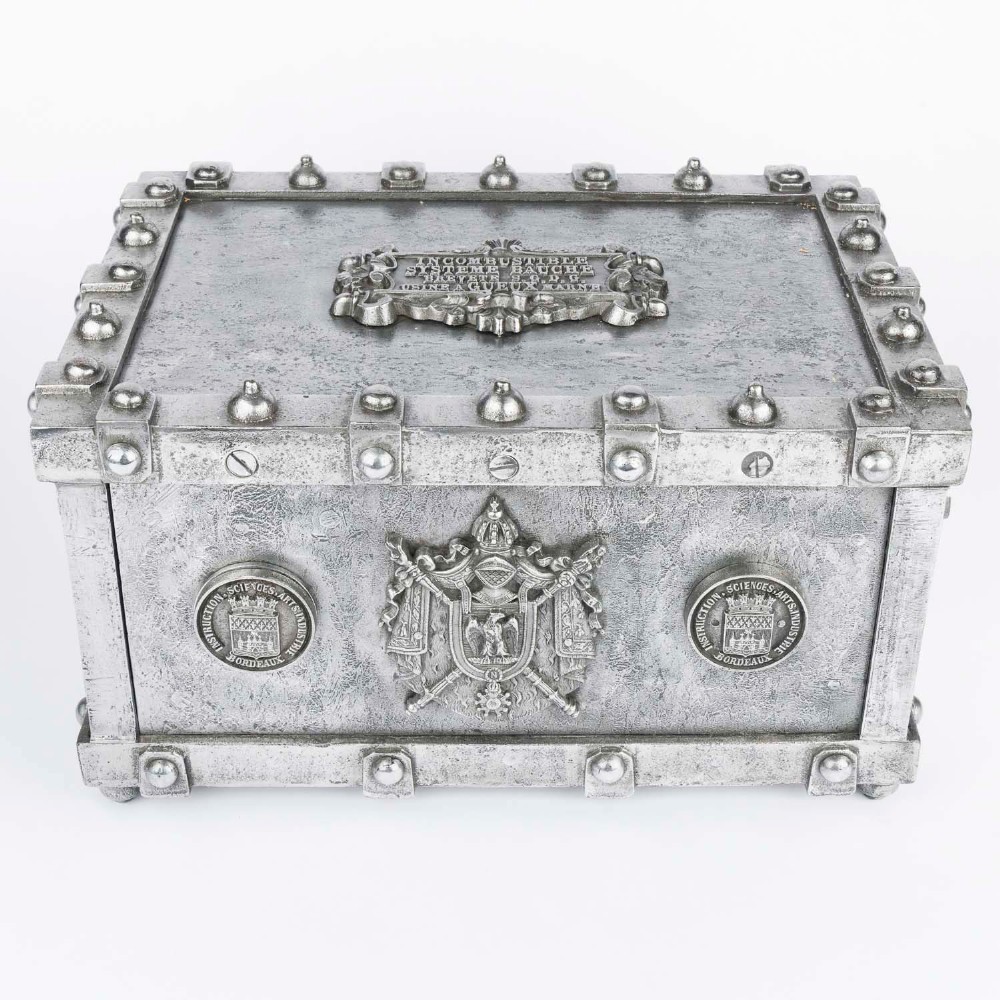 A heavy rectangular metal strongbox featuring riveted steel straps, raised studs, an embossed coat of arms, and maker plaques.