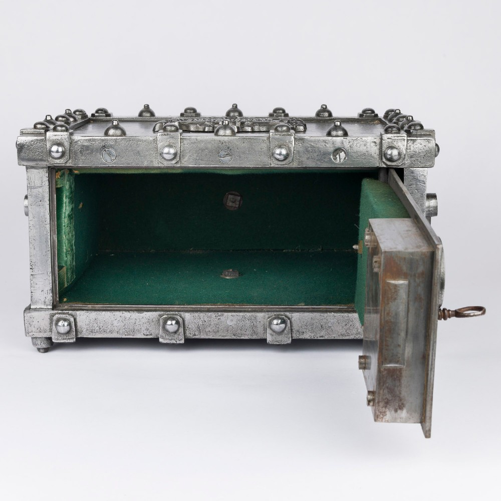 A heavy rectangular metal strongbox featuring riveted steel straps, raised studs, an embossed coat of arms, and maker plaques. View VII