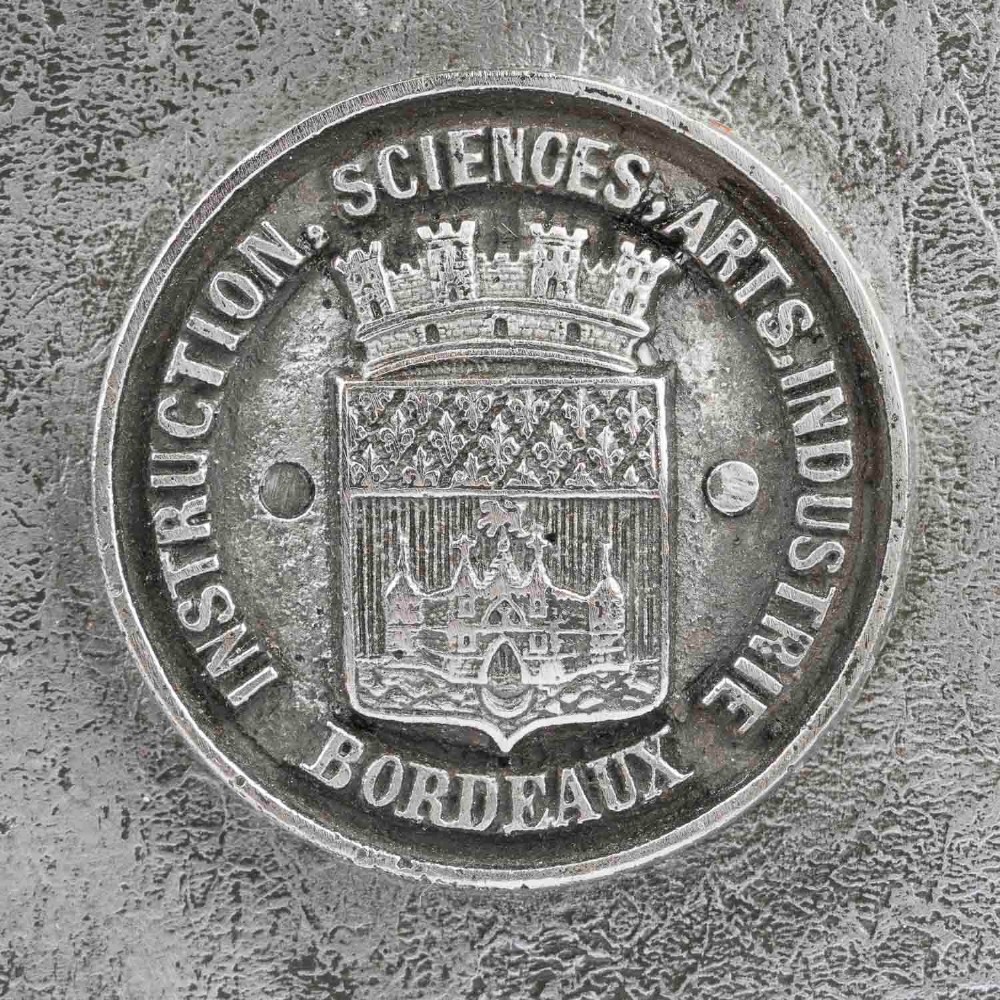 A heavy rectangular metal strongbox featuring riveted steel straps, raised studs, an embossed coat of arms, and maker plaques. View IX