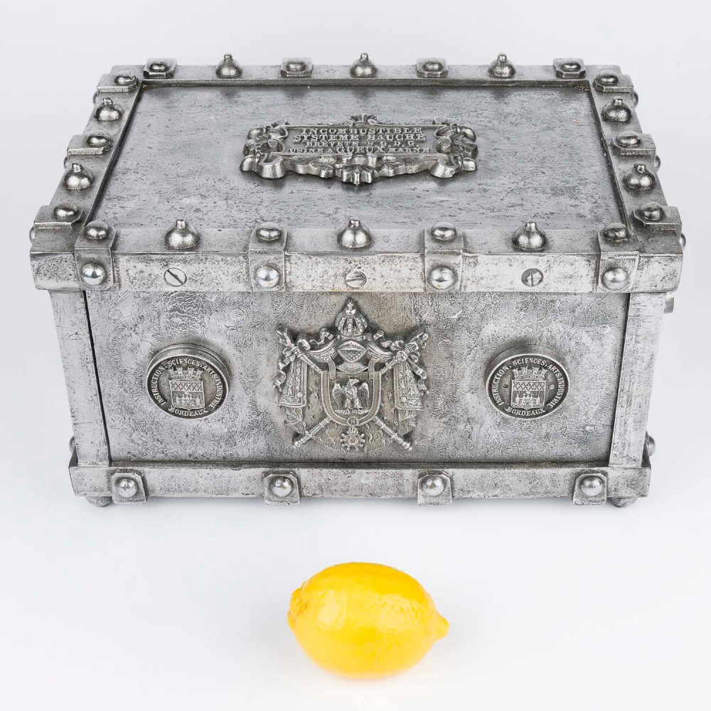 A heavy rectangular metal strongbox featuring riveted steel straps, raised studs, an embossed coat of arms, and maker plaques. View XIII
