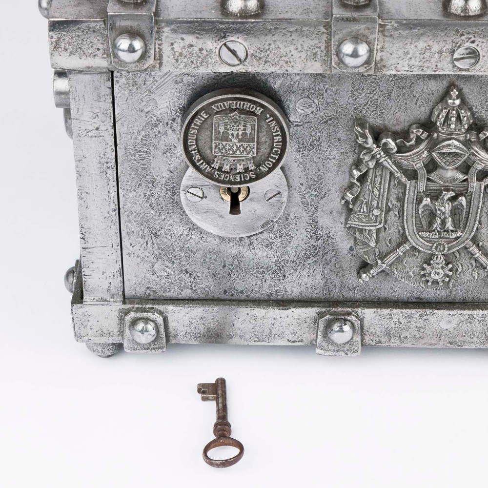 A heavy rectangular metal strongbox featuring riveted steel straps, raised studs, an embossed coat of arms, and maker plaques. View XIV