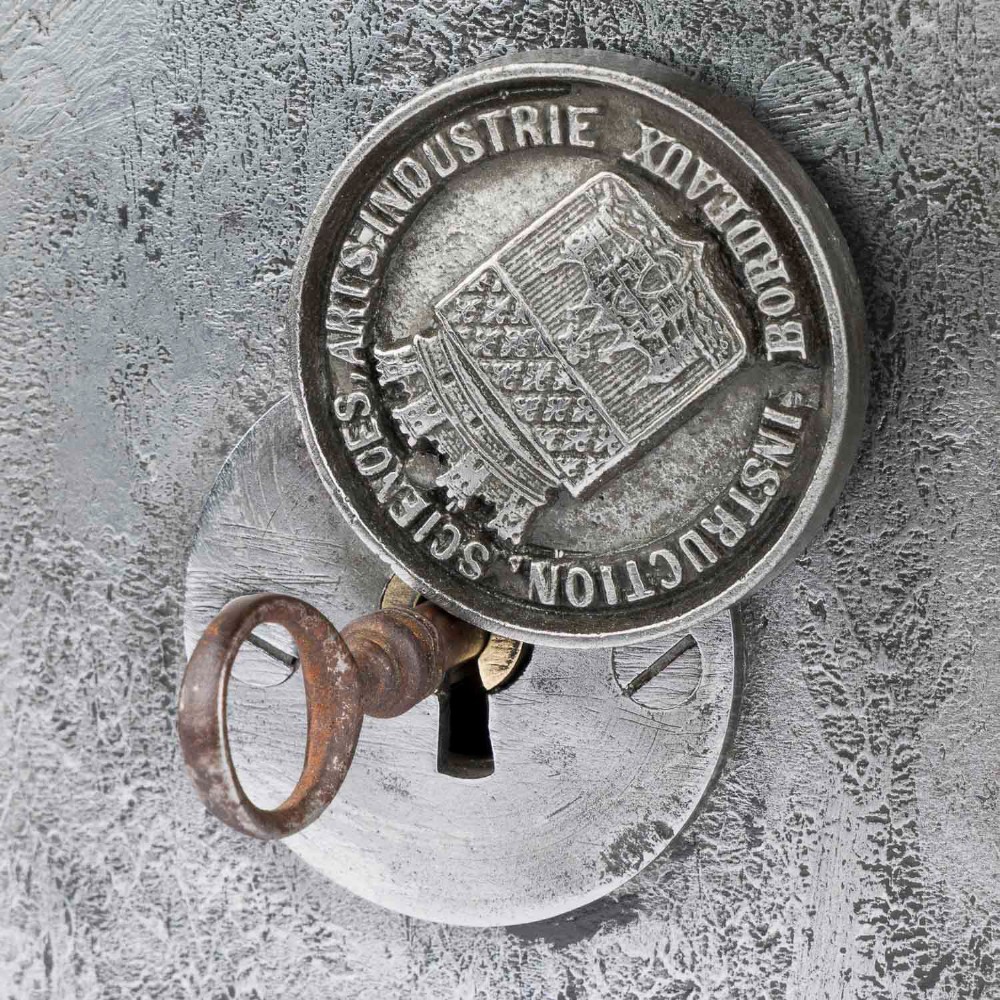 A heavy rectangular metal strongbox featuring riveted steel straps, raised studs, an embossed coat of arms, and maker plaques. View XV