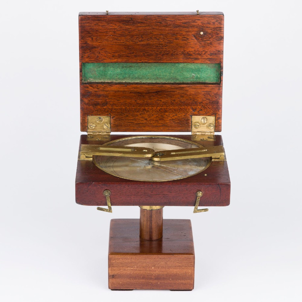 An antique mahogany cased surveyor compass with folding brass sight vanes and a circular glass-covered needle face, mounted on a wooden pedestal base. View III