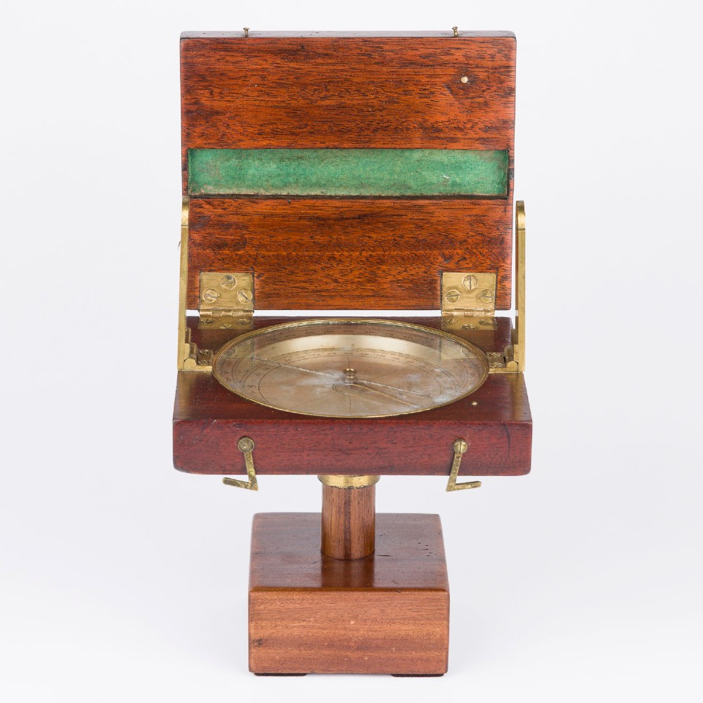An antique mahogany cased surveyor compass with folding brass sight vanes and a circular glass-covered needle face, mounted on a wooden pedestal base. View VI