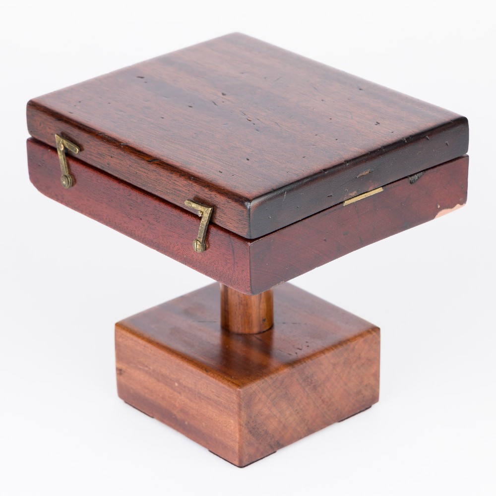 An antique mahogany cased surveyor compass with folding brass sight vanes and a circular glass-covered needle face, mounted on a wooden pedestal base. View IX