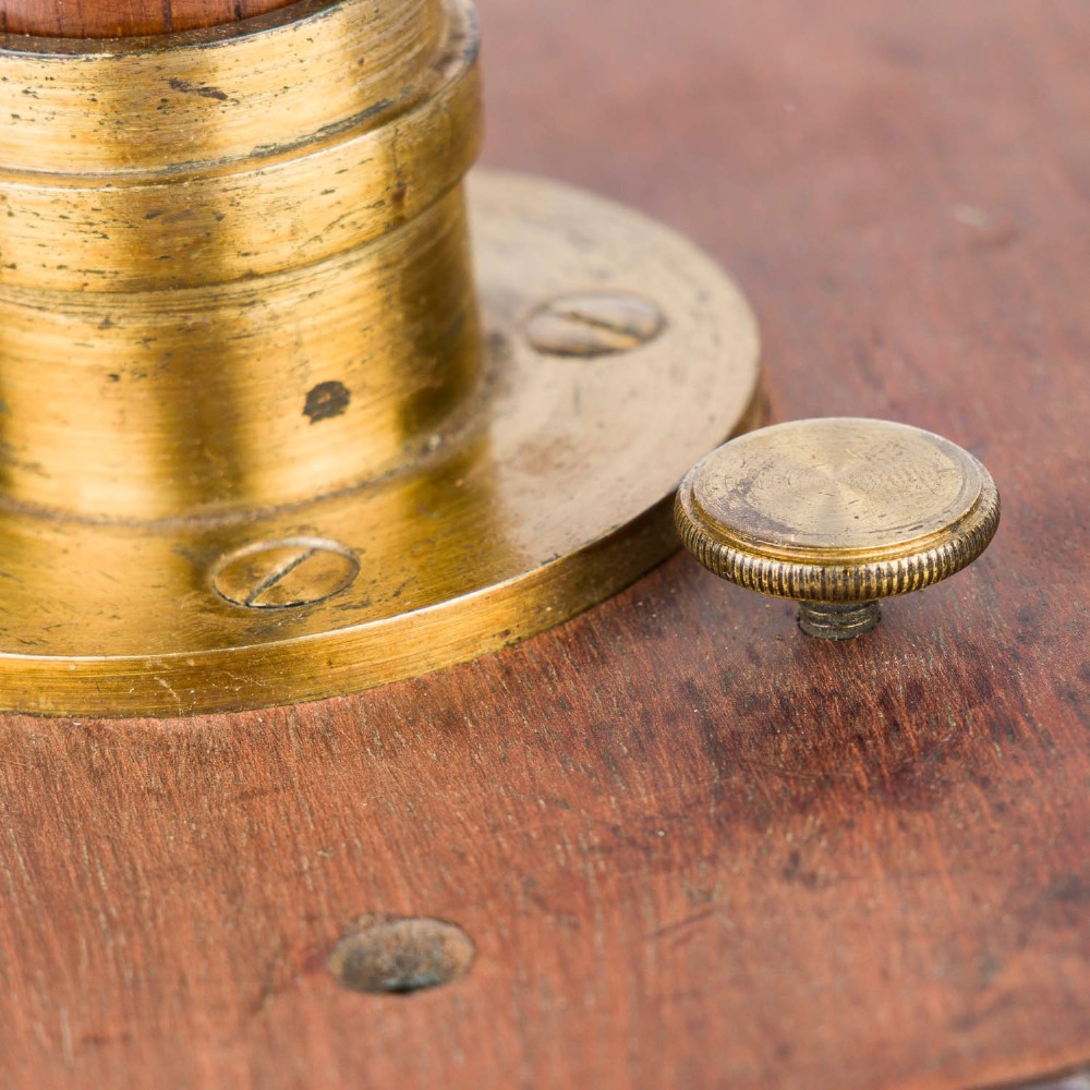 An antique mahogany cased surveyor compass with folding brass sight vanes and a circular glass-covered needle face, mounted on a wooden pedestal base. View XI