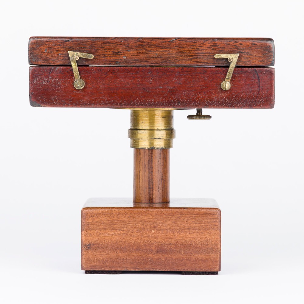 An antique mahogany cased surveyor compass with folding brass sight vanes and a circular glass-covered needle face, mounted on a wooden pedestal base. View XII