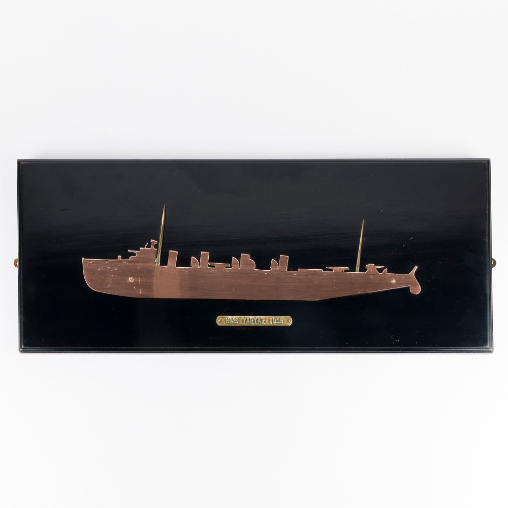 A rectangular black lacquered wooden plaque displaying a copper cutout profile of HMS Tartar 1906 with a small brass title tag below.