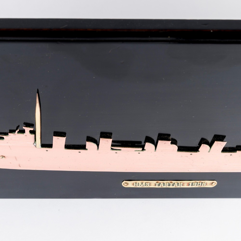 A rectangular black lacquered wooden plaque displaying a copper cutout profile of HMS Tartar 1906 with a small brass title tag below. View III
