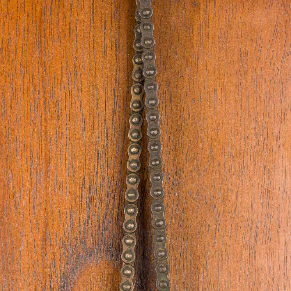 An antique brass engine room telegraph with two dials connected by a chain on a tall, arched timber backboard. View VII