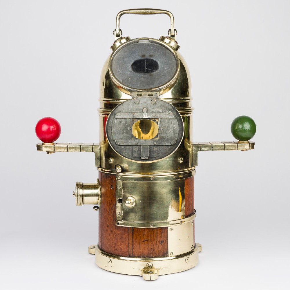 A polished brass and mahogany submarine binnacle featuring a hinged hood with carrying handle, a glass viewing lens, and extended side arms holding red and green painted iron spheres. View II