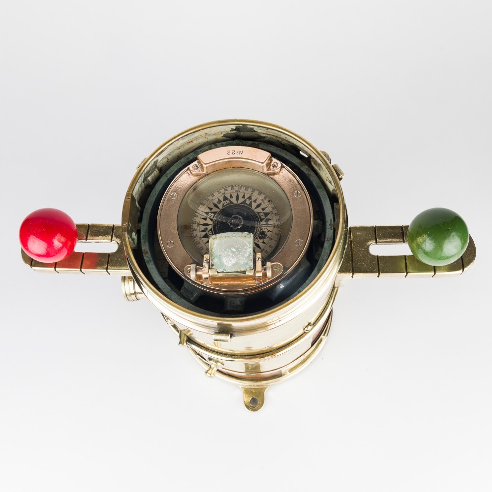 A polished brass and mahogany submarine binnacle featuring a hinged hood with carrying handle, a glass viewing lens, and extended side arms holding red and green painted iron spheres. View VII