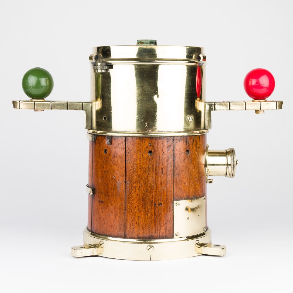 A polished brass and mahogany submarine binnacle featuring a hinged hood with carrying handle, a glass viewing lens, and extended side arms holding red and green painted iron spheres. View IX
