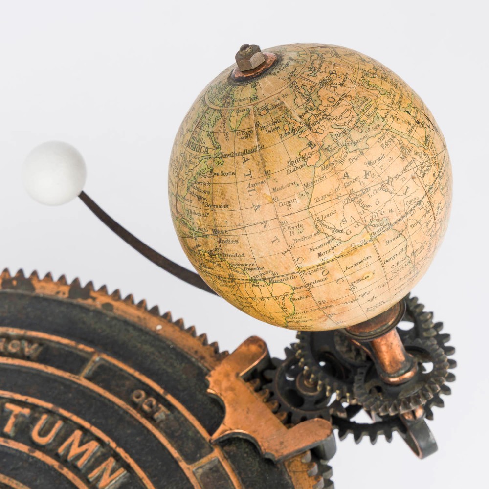 A Victorian Parkes and Hadley patent tellurian orrery featuring a cast metal base with calendar markings, interlocking gears, and a small terrestrial globe with a moon attachment. View VIII