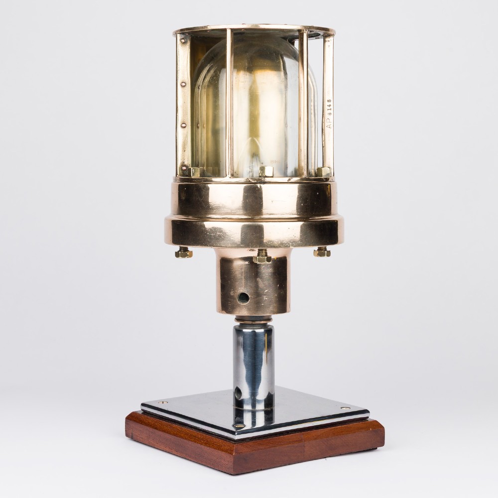 A polished brass submarine steaming light featuring a clear glass dome encased in a protective metal cage, mounted on a chrome stem and wooden plinth. View II
