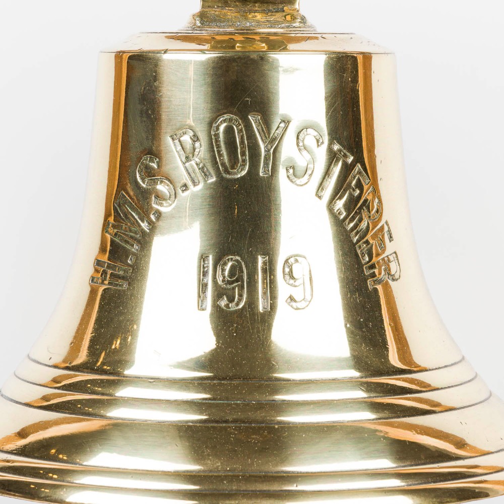 A polished brass Royal Navy ships bell engraved HMS Roysterer 1919, suspended inside a light oak wooden frame. View II