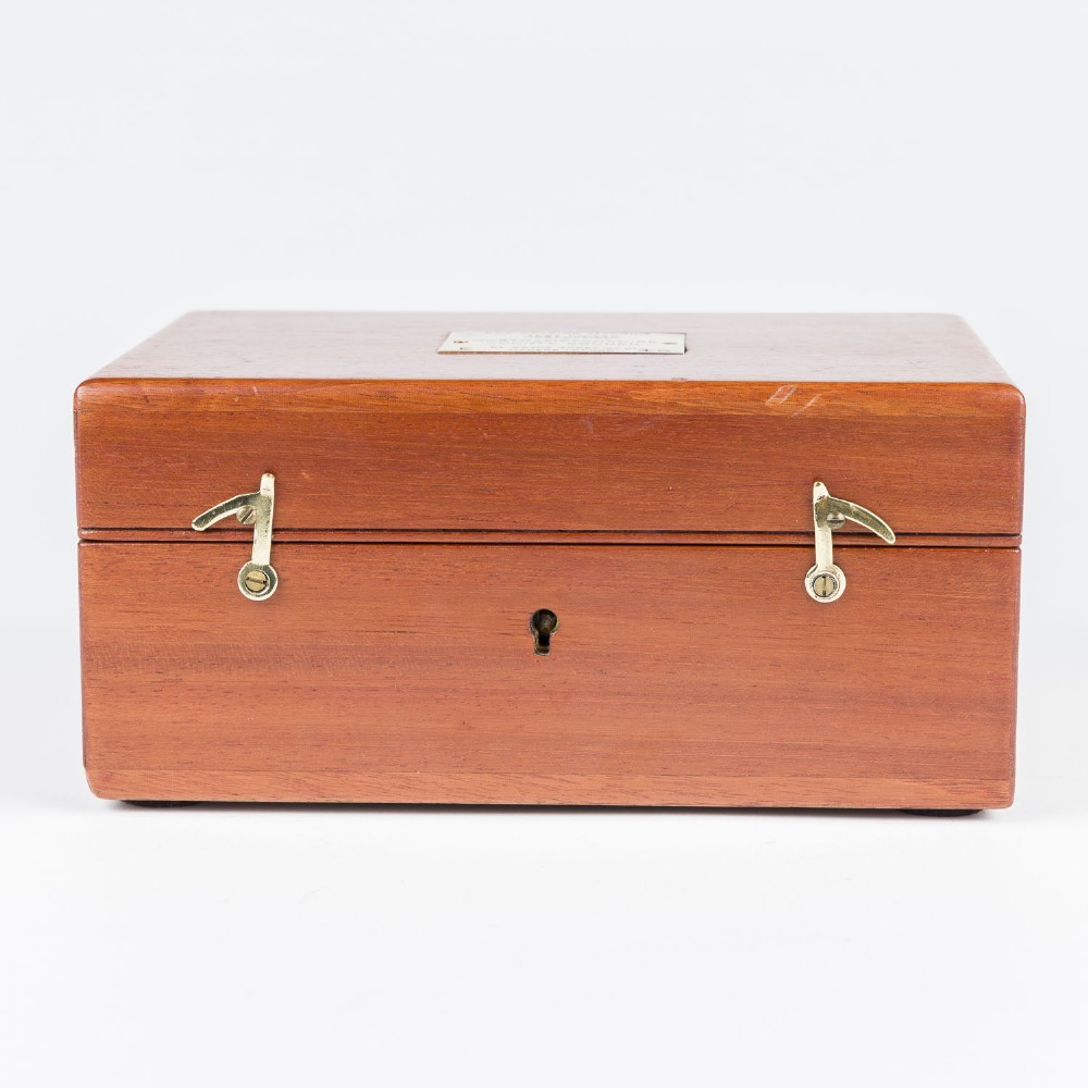 An open mahogany wooden box lined with blue velvet, containing six rounded metal egg weights and brass tweezers fitted into the lid. View VI