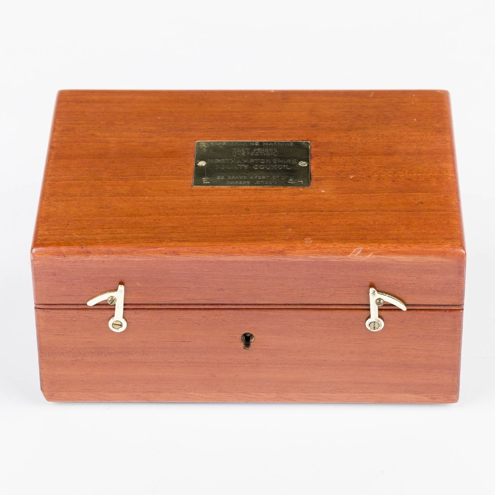 An open mahogany wooden box lined with blue velvet, containing six rounded metal egg weights and brass tweezers fitted into the lid. View VII