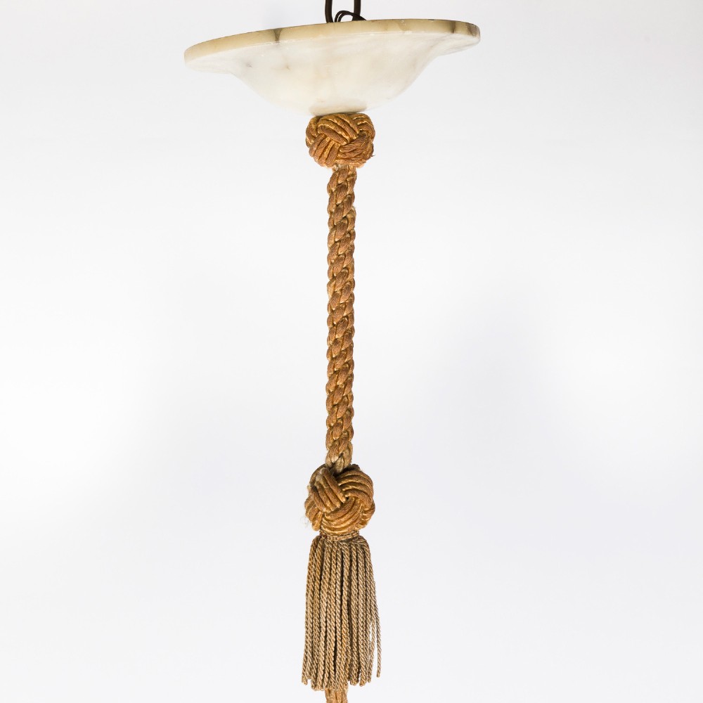 A fluted white alabaster urn-shaped light shade suspended by decorative woven cords and tassels from a matching alabaster ceiling rose. View IV