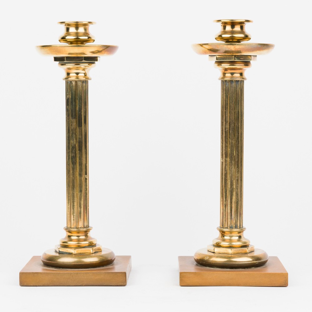 A pair of polished bronze Art Deco candlesticks featuring fluted vertical columns and stepped square plinth bases.