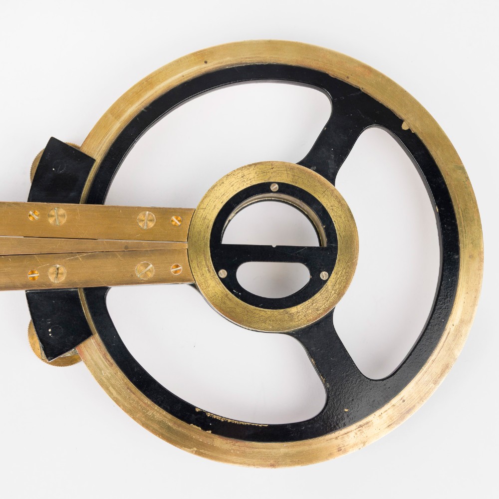 An antique brass and black lacquered three-arm station pointer with a circular graduated dial and precision adjustment knobs. View V
