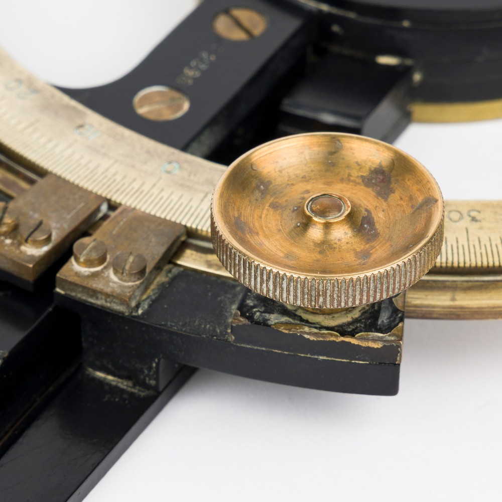 An antique brass and black lacquered three-arm station pointer with a circular graduated dial and precision adjustment knobs. View VI