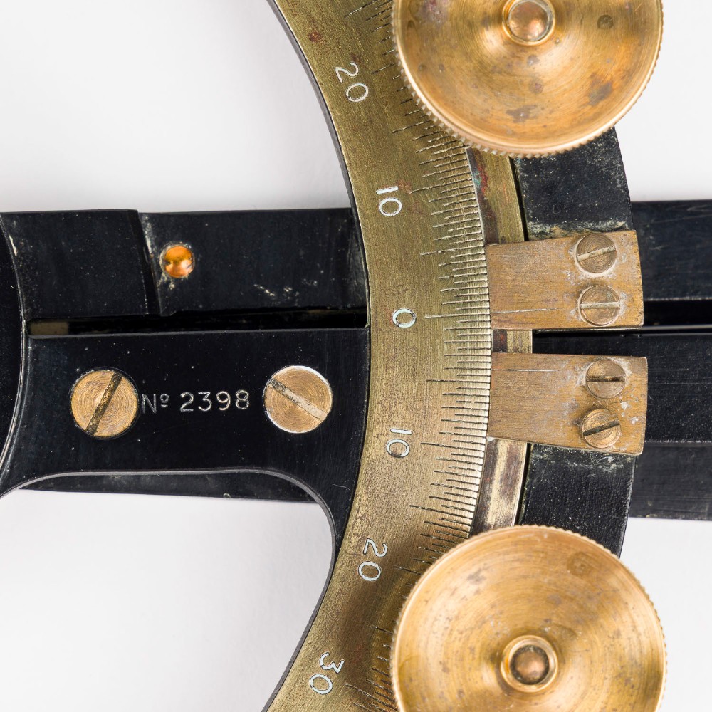 An antique brass and black lacquered three-arm station pointer with a circular graduated dial and precision adjustment knobs. View VII