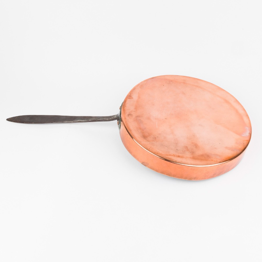 A circular antique copper saute pan with a dark tin-lined interior and a long dark iron handle. View II