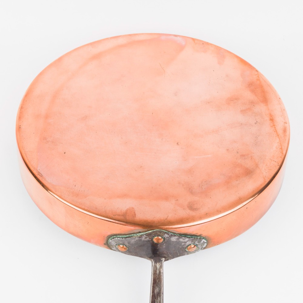 A circular antique copper saute pan with a dark tin-lined interior and a long dark iron handle. View III