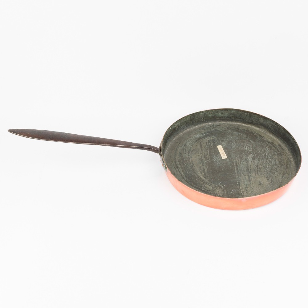 A circular antique copper saute pan with a dark tin-lined interior and a long dark iron handle. View V