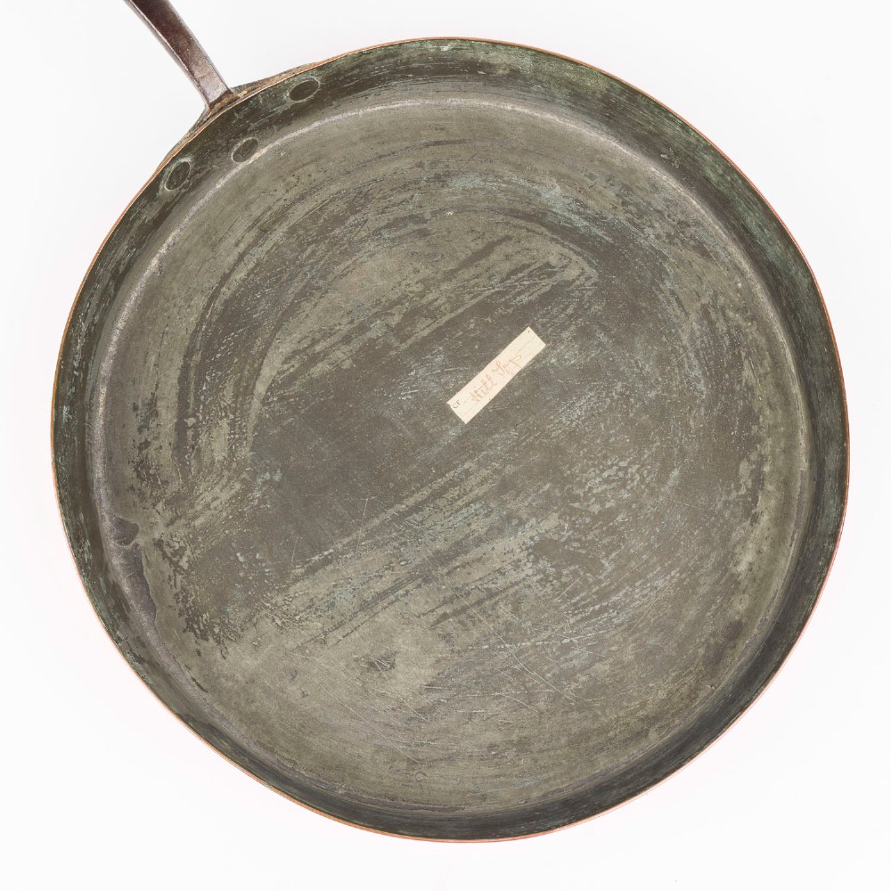 A circular antique copper saute pan with a dark tin-lined interior and a long dark iron handle. View VI