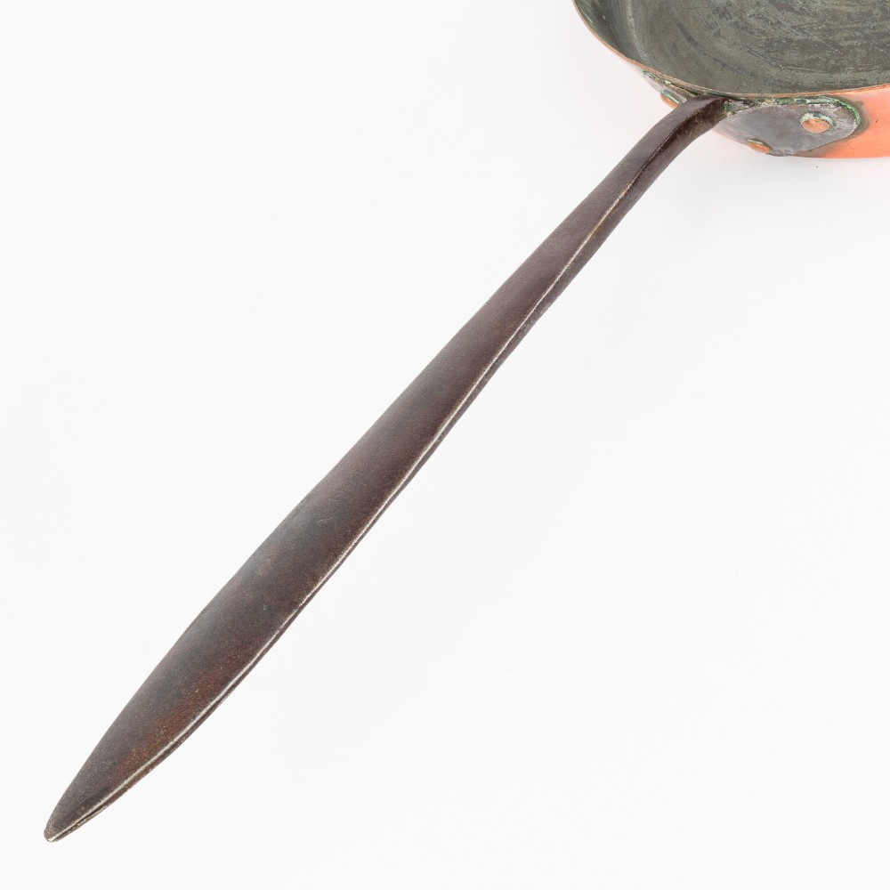 A circular antique copper saute pan with a dark tin-lined interior and a long dark iron handle. View VIII