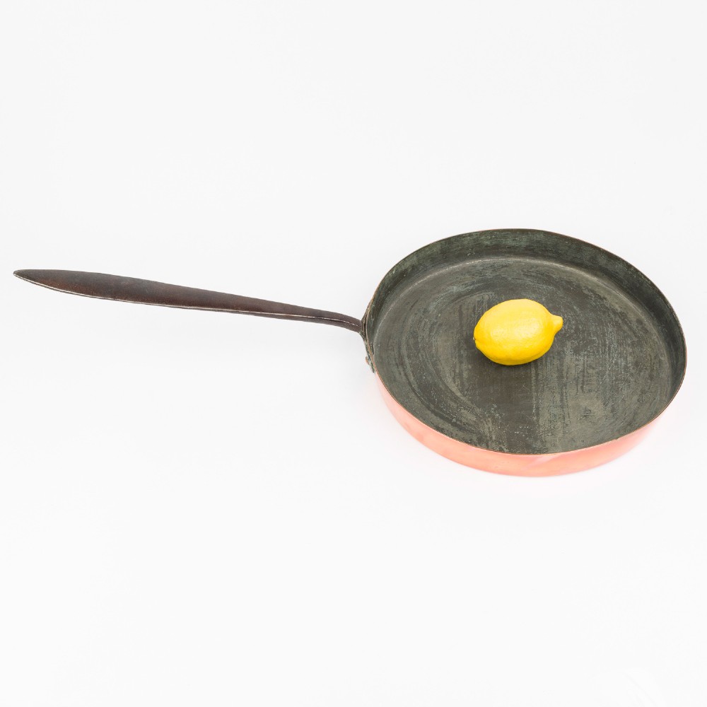 A circular antique copper saute pan with a dark tin-lined interior and a long dark iron handle. View IX