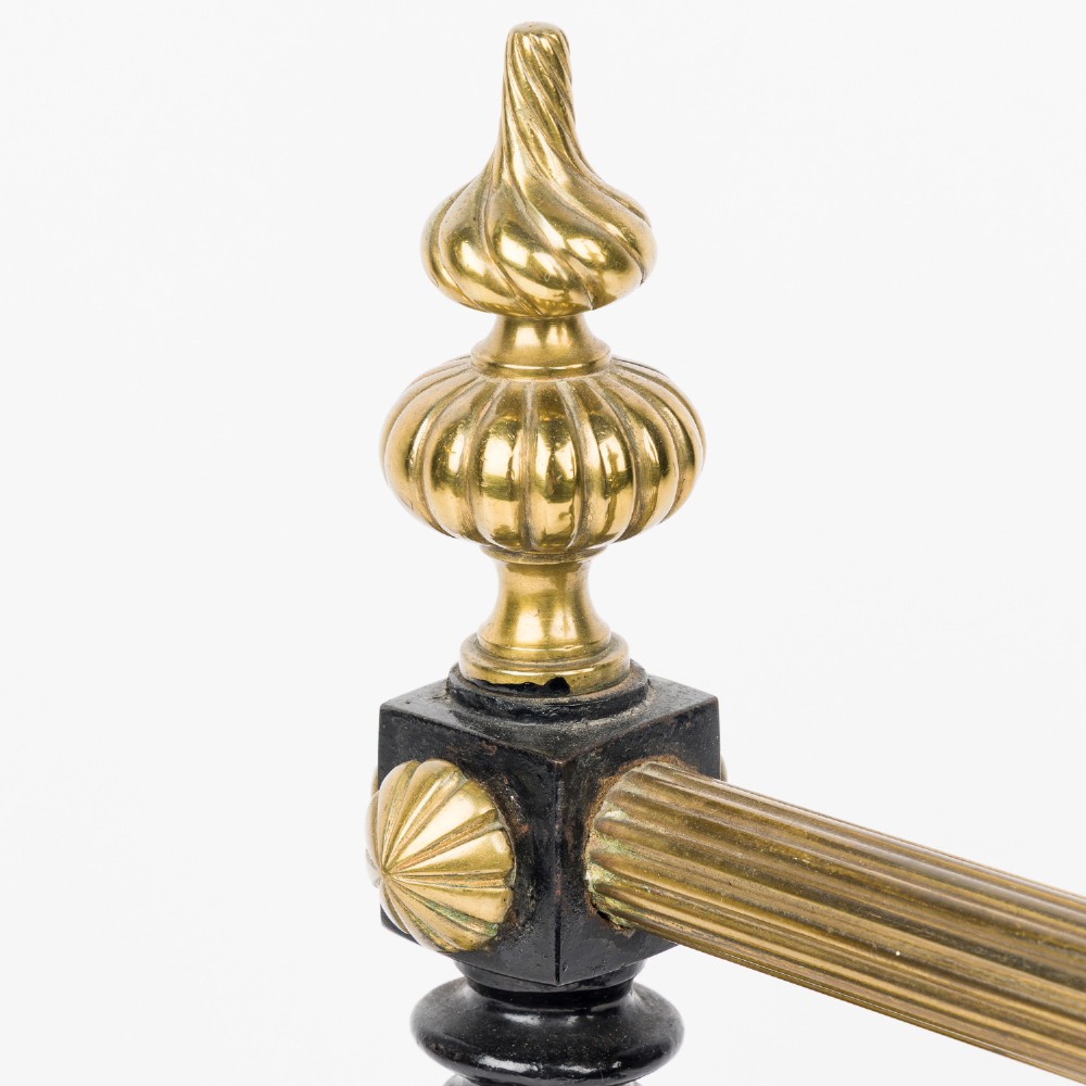A pair of cast iron and brass fire dogs with ornate brass urn finials, fluted central bars, and black scroll feet. View V