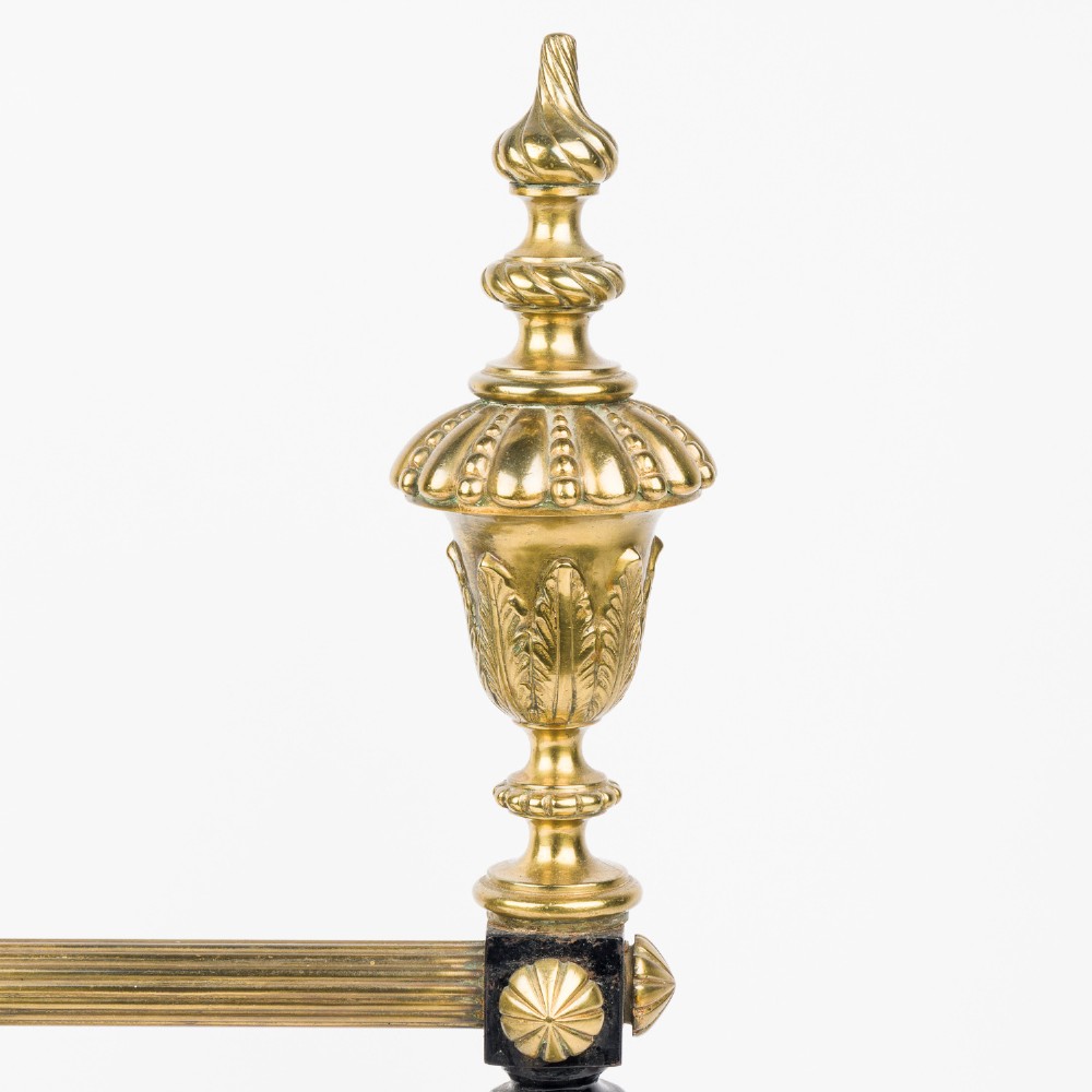 A pair of cast iron and brass fire dogs with ornate brass urn finials, fluted central bars, and black scroll feet. View VI
