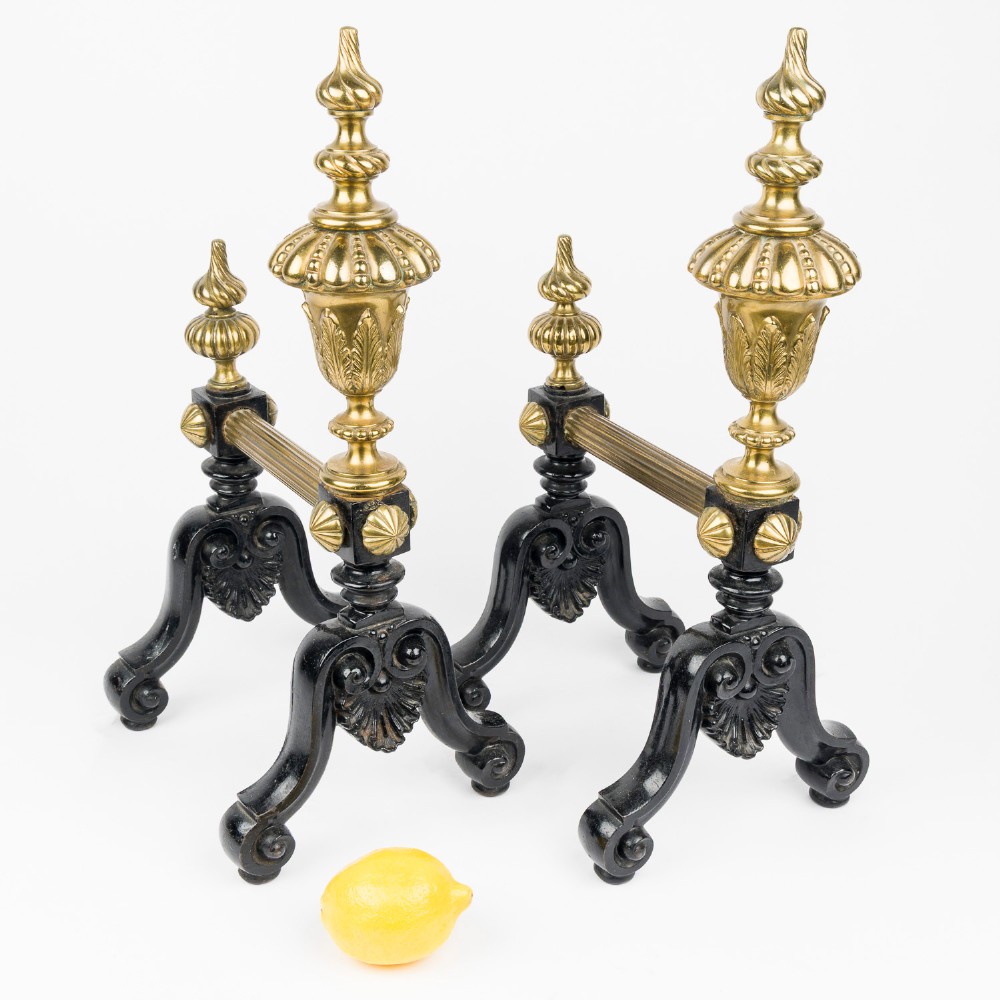 A pair of cast iron and brass fire dogs with ornate brass urn finials, fluted central bars, and black scroll feet. View VIII