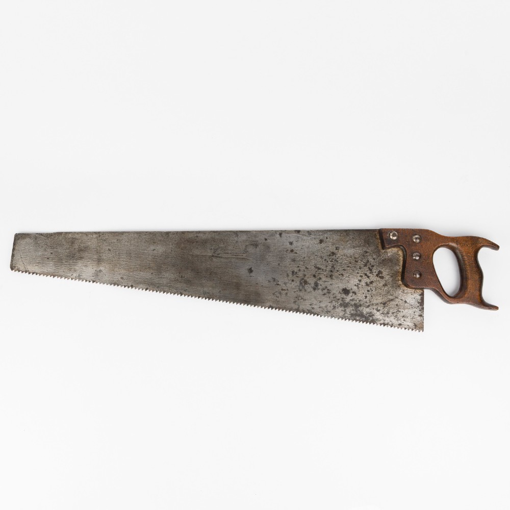 An antique steel hand saw featuring a patinated blade with visible teeth and a shaped wooden handle secured with metal rivets.