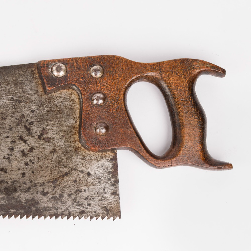An antique steel hand saw featuring a patinated blade with visible teeth and a shaped wooden handle secured with metal rivets. View II
