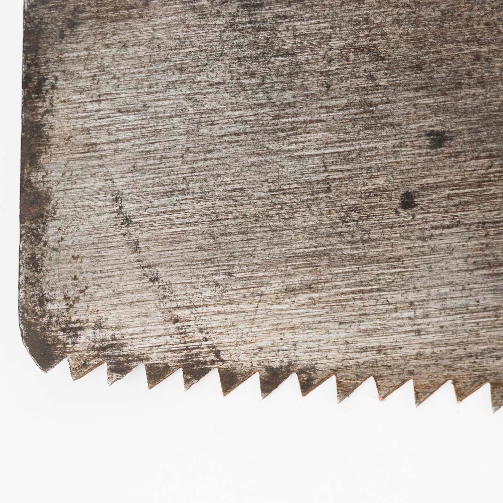 An antique steel hand saw featuring a patinated blade with visible teeth and a shaped wooden handle secured with metal rivets. View IV