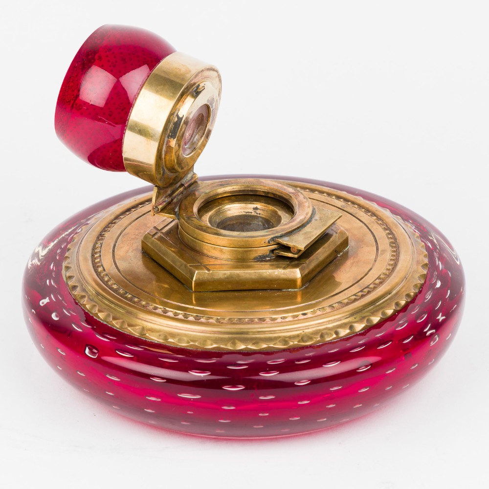 A circular ruby red glass inkwell featuring a controlled bubble pattern with a brass collar and matching glass stopper. View II