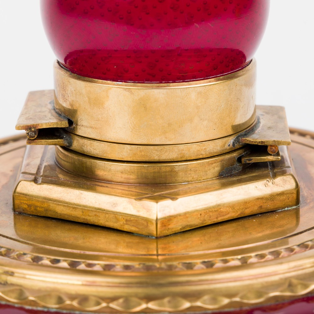 A circular ruby red glass inkwell featuring a controlled bubble pattern with a brass collar and matching glass stopper. View IV