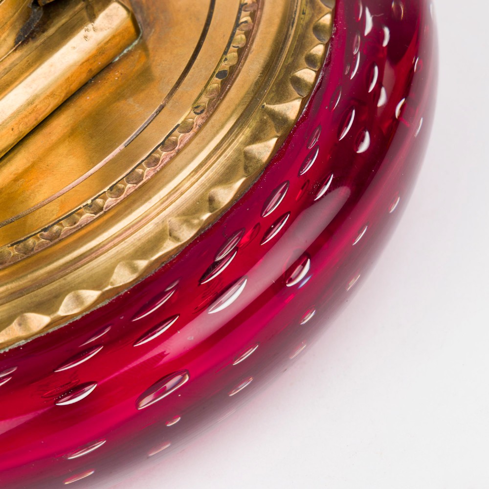 A circular ruby red glass inkwell featuring a controlled bubble pattern with a brass collar and matching glass stopper. View VII