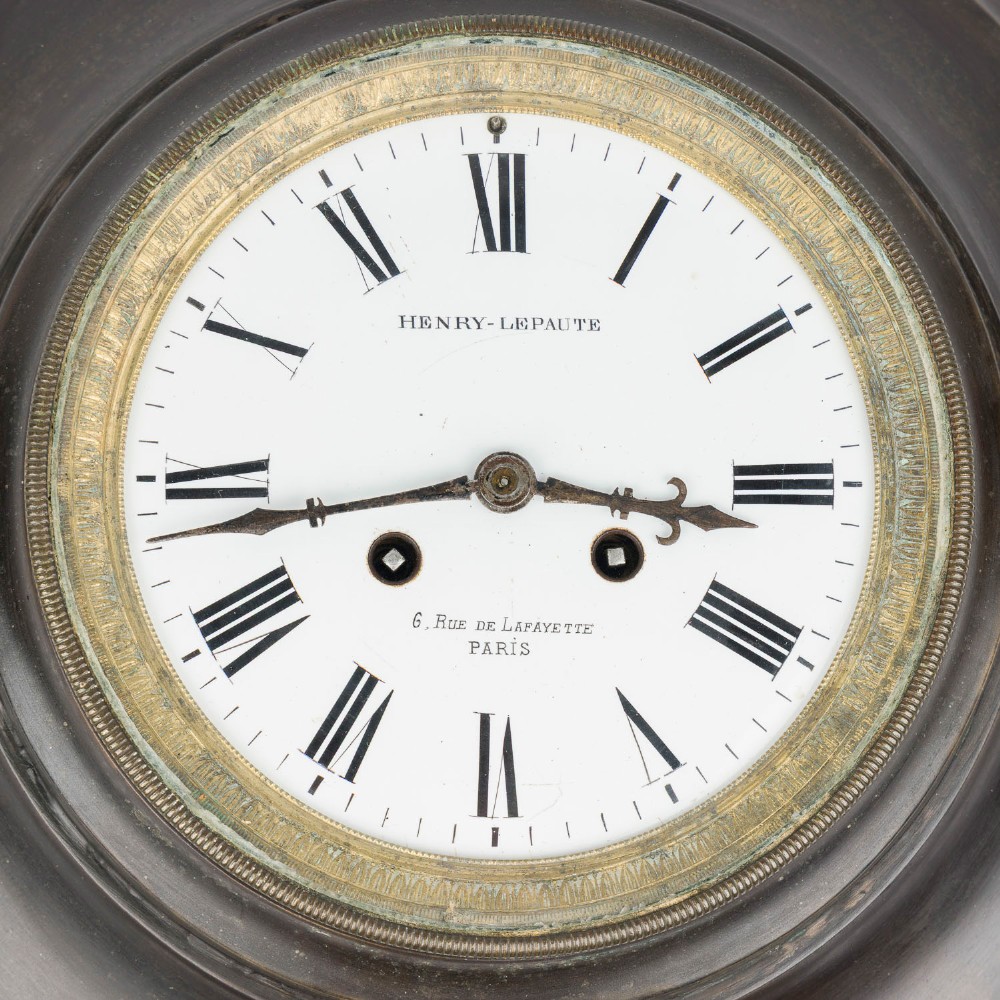 A circular dark bronze French wall clock designed in the shape of a pocket watch with a white enamel dial and Roman numerals. View II