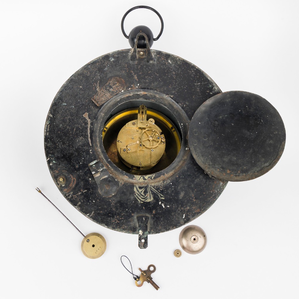 A circular dark bronze French wall clock designed in the shape of a pocket watch with a white enamel dial and Roman numerals. View VII